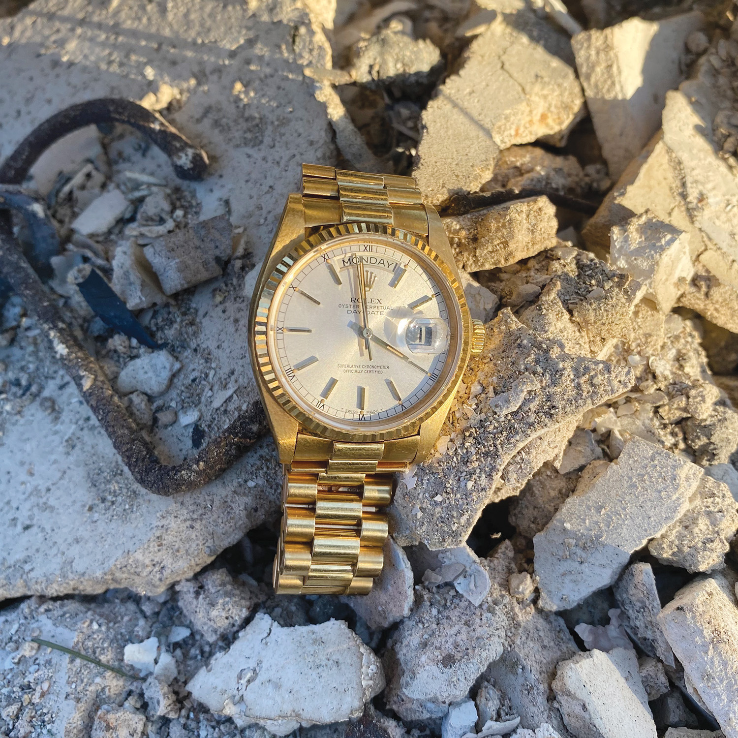 A gold Rolex watch nestled in rubble from a fire